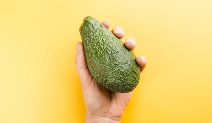 Avocado in einer Hand vor gelbem Hintergrund