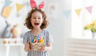 Mädchen mit Hasenohrenhaarreif hält ein Osterkorb mit bunten Eiern in der Hand
