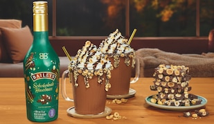 Baileys Schokolade Haselnuss Flasche, daneben zwei Tassen mit Sahne.png