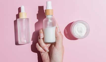 Beauty Produkte vor pinkem Hintergrund werden von einer Frauenhand gegriffen
