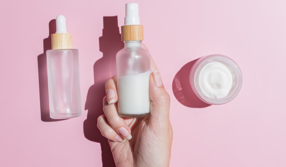 Beauty Produkte vor pinkem Hintergrund werden von einer Frauenhand gegriffen