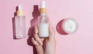 Beauty Produkte vor pinkem Hintergrund werden von einer Frauenhand gegriffen