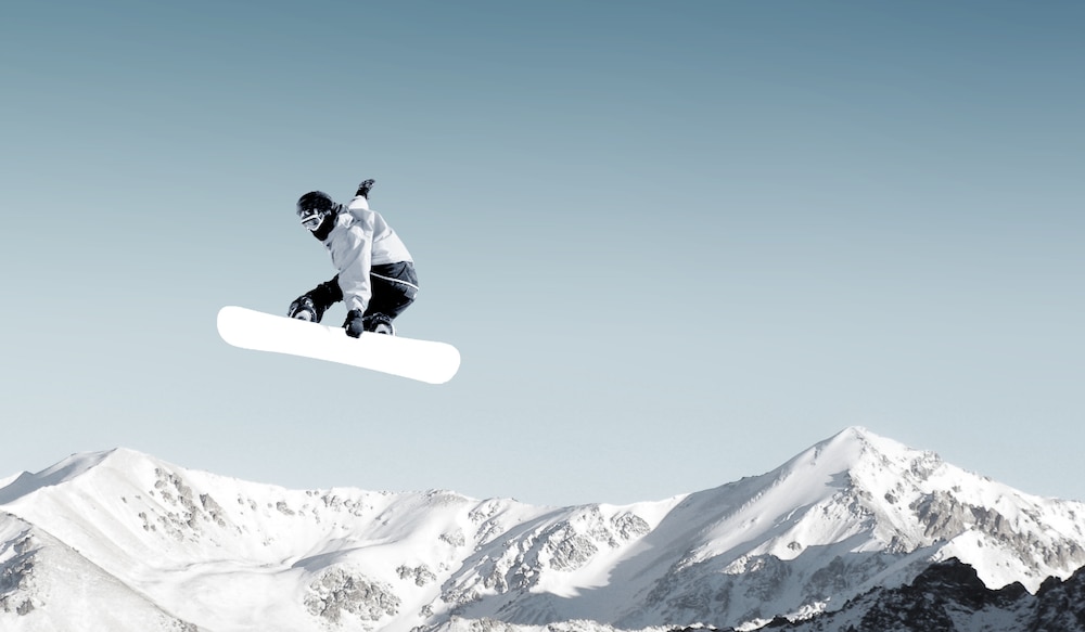 Berge, blauer Himmel, Person mit Snowboard in der Luft.