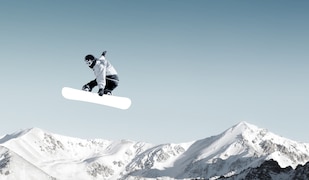 Berge, blauer Himmel, Person mit Snowboard in der Luft.