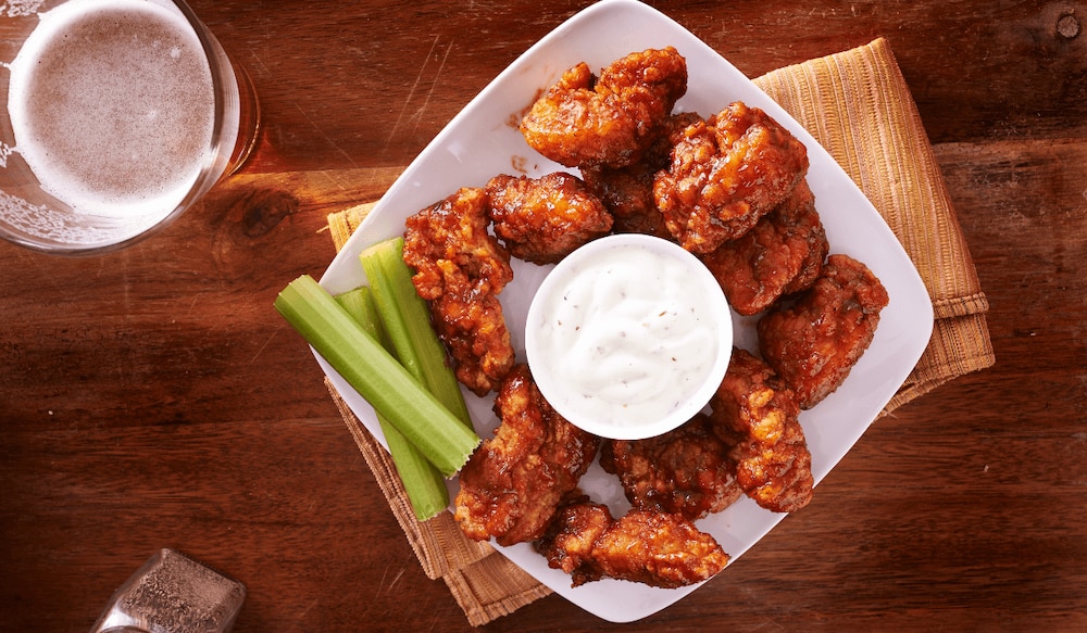 Buffalo Hot Wings auf einem Teller mit Dip, Bier und Sellerie