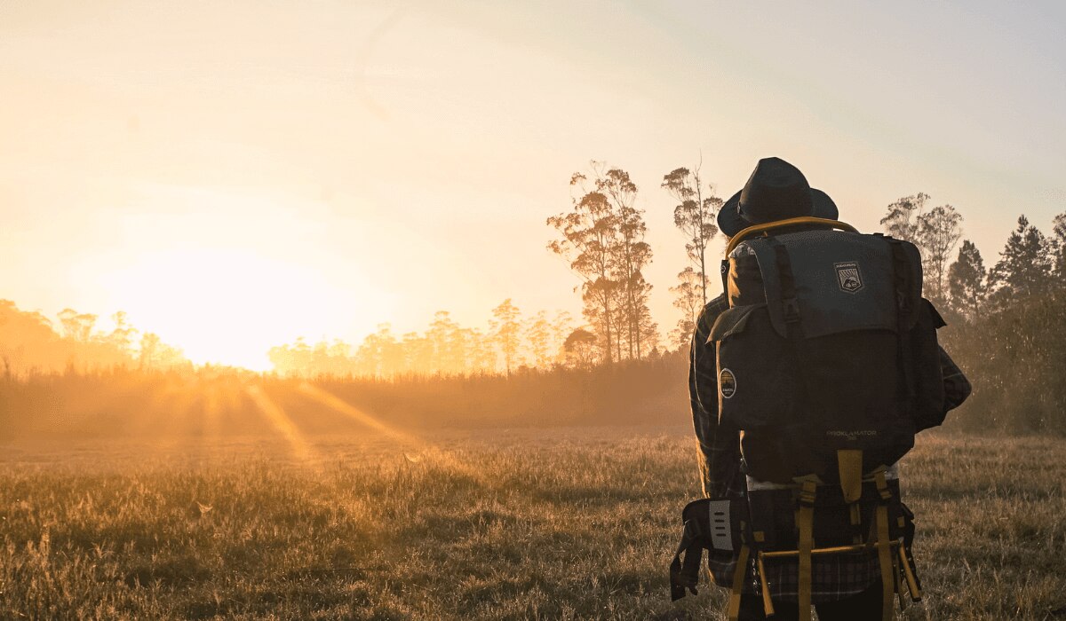 Camper bei Sonnenaufgang mit Rucksack in der Natur