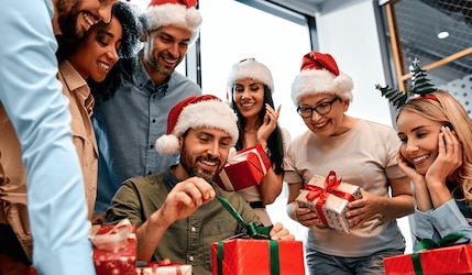 Damen und Herren packen gegenseitig Wichtelgeschenke zu Weihnachten aus