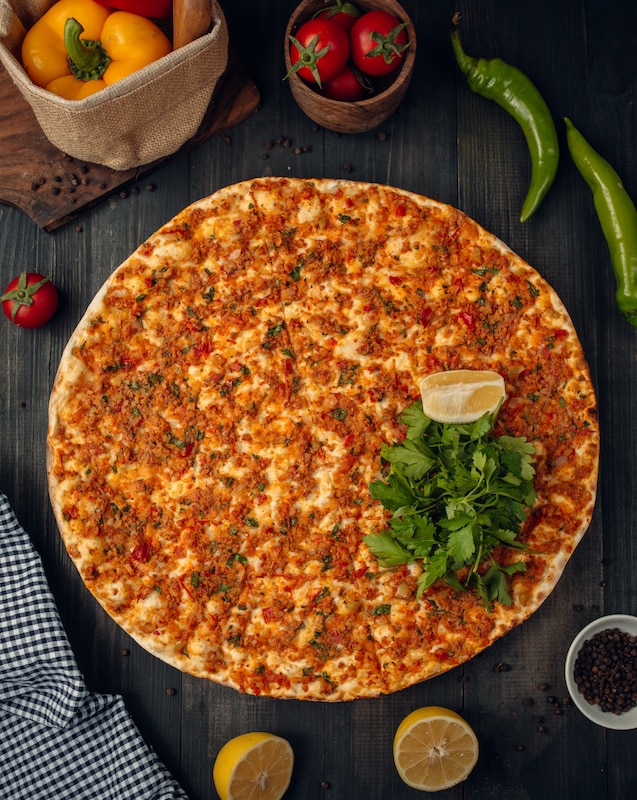 Traditioneller Lahmacun mit dünnem Fladenbrot, würziger Hackfleisch-Tomaten-Mischung, garniert mit frischer Petersilie und Zitronenspalte, auf dunklem Holztisch serviert.