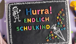 Kuchen, der aussieht wie eine Schultafel mit dem Schriftzug "Hurra! Endlich Schulkind" und bunter Dekoration