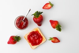Erdbeermarmelade in einem Einmachglas mit frischen Erdbeeren daneben