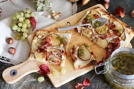 Flammkuchen mit Birne, Trauben, Speck und Haselnüssen auf einem Holzbrett