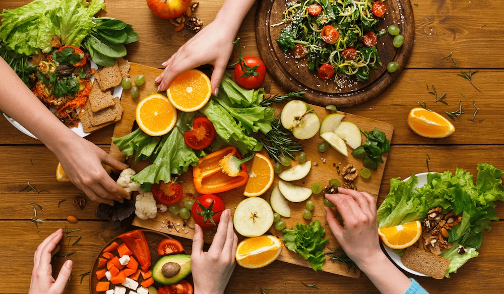 Gesundes Essen auf Holzplatte und 5 Hände, die danach greifen