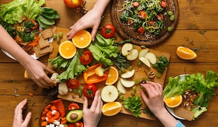 Gesundes Essen auf Holzplatte und 5 Hände, die danach greifen