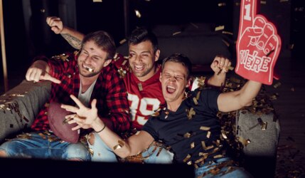 Football Fans jubeln vor einem Fernseher mit Football Deko und Trikots