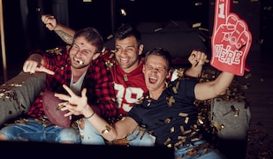 Football Fans jubeln vor einem Fernseher mit Football Deko und Trikots