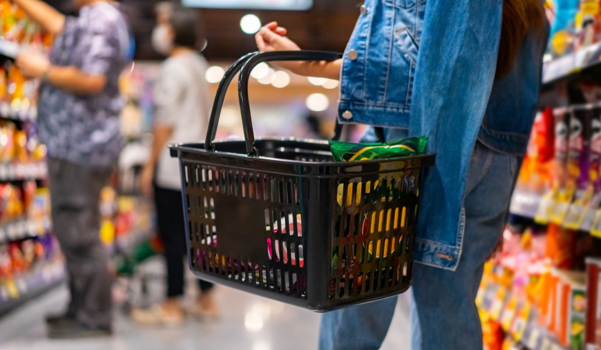 Frau geht mit einem Einkaufskorb in der Hand durch einen Supermarkt und kauft ein