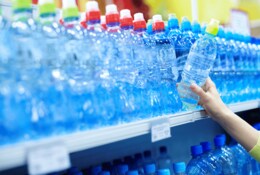 Frau greift nach einer Wasserflasche im Supermarkt