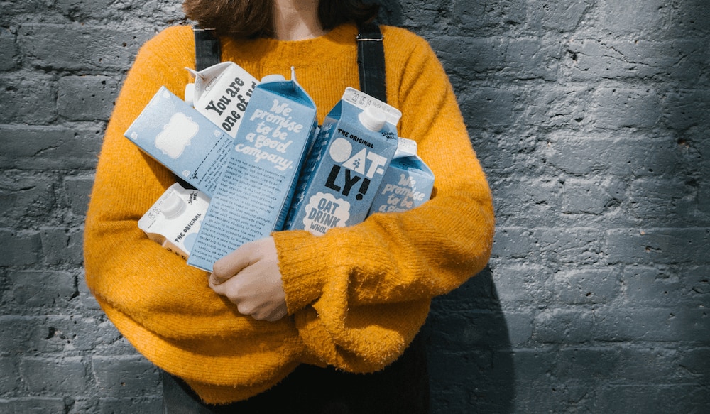 Frau in gelbem Pullover trägt viele Oatly Produkte