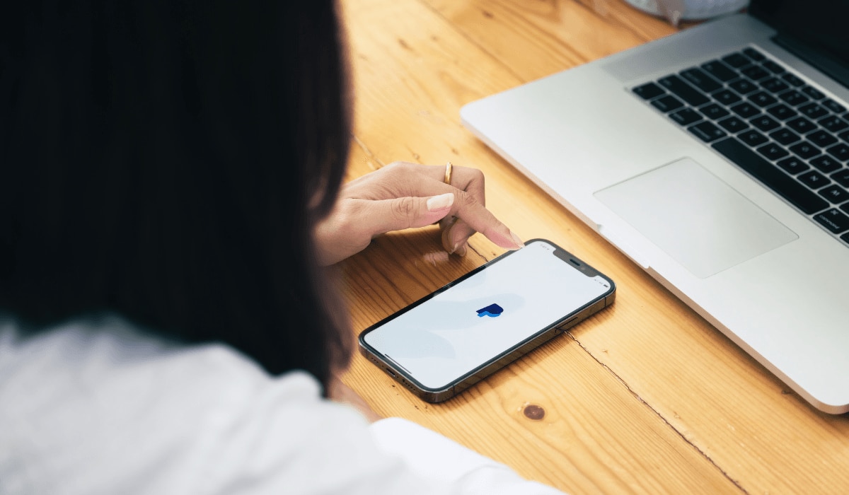 Frau nutzt die PayPal-App auf einem Smartphone vor einem Laptop