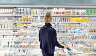Frau steht im Supermarkt vor dem Molkereiprodukte Regal