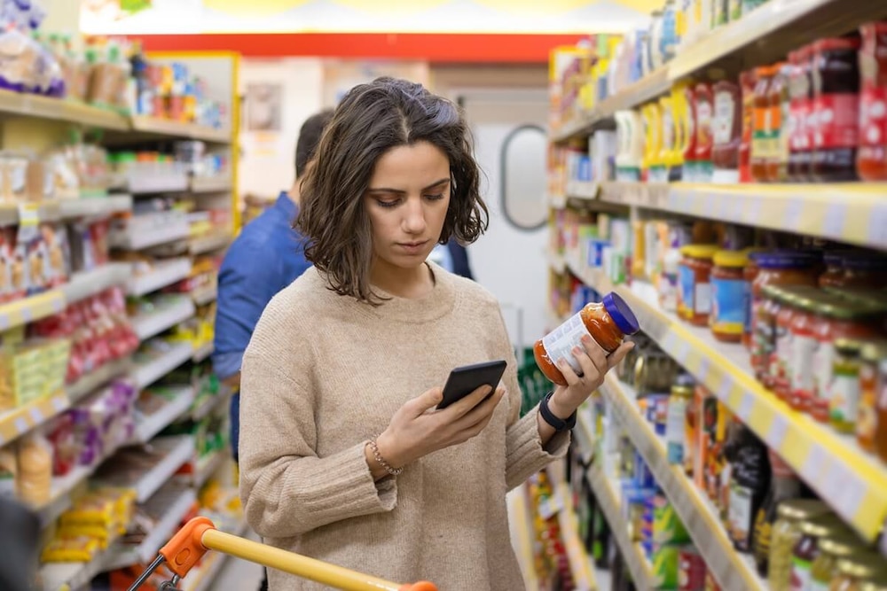 Frau im Supermarkt checkt Produkt mit Smartphone