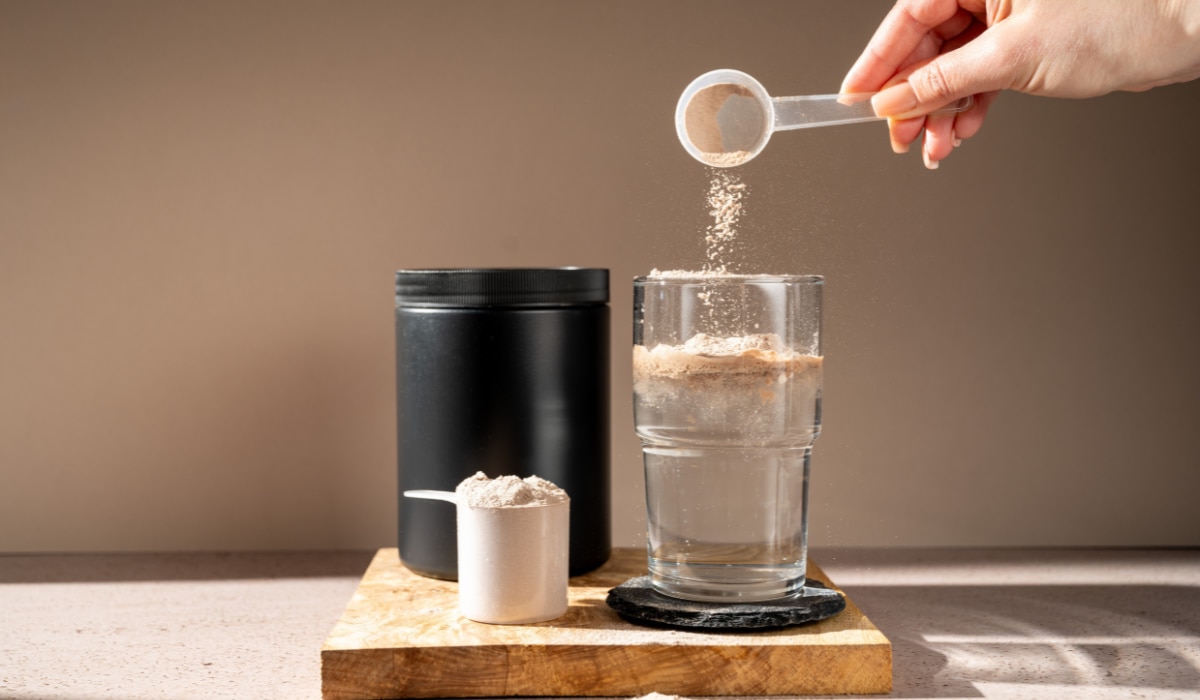 Getränkepulver wird mit einem Messlöffel in ein Glas Wasser gegeben.png
