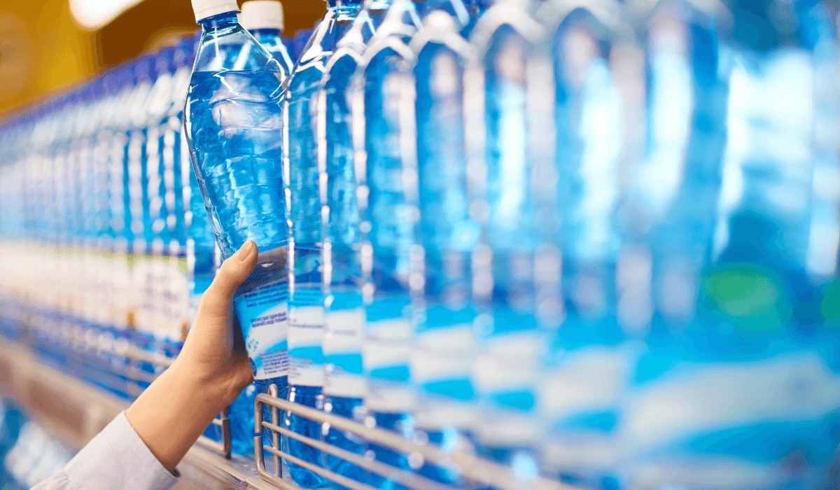 Hand greift im Supermarkt zu einer Flasche Wasser im Regal