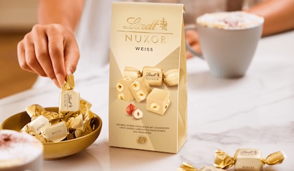 Hand greift zu Lindt Nuxor weiß einzeln verpackt und in der großen Verpackung