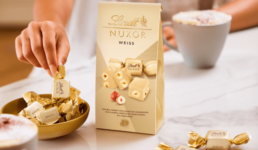 Hand greift zu Lindt Nuxor weiß einzeln verpackt und in der großen Verpackung