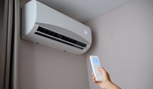 Hand häkt eine Fernbedienung mit der eine Klimaanlage an einer Wand gesteuert wird