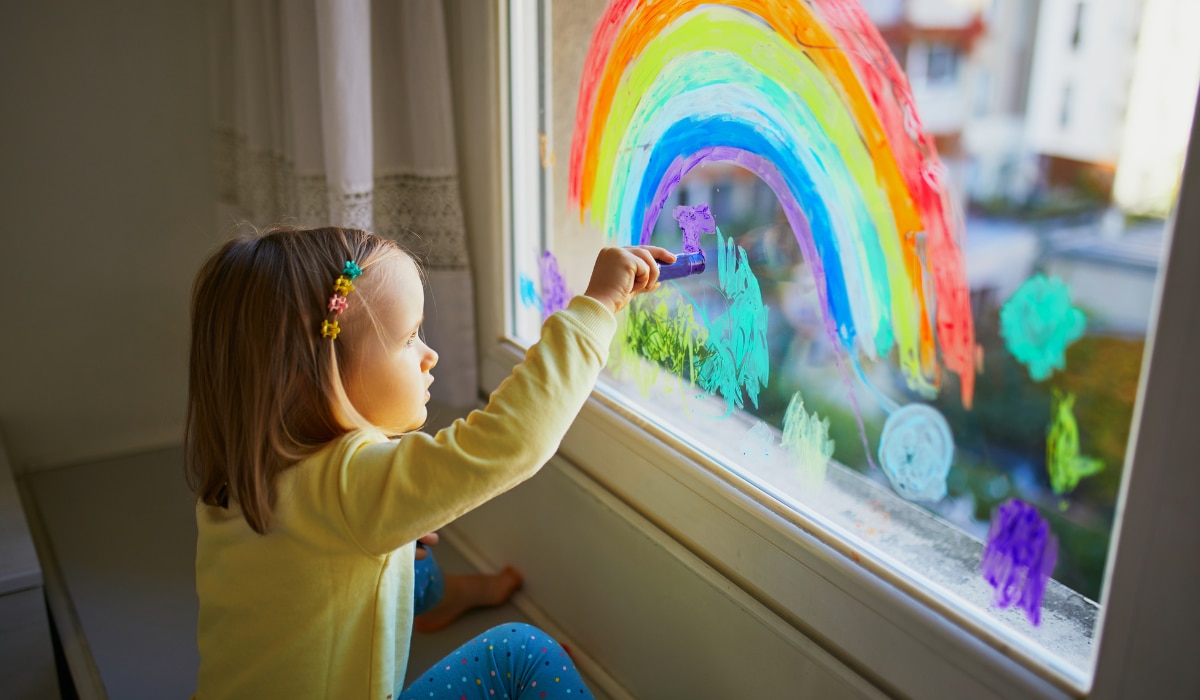 Kind malt Regenbogen auf das Fenster