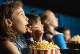 Kinder sitzen gespannt in einem Kino und essen Popcorn