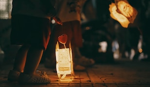 Kind mit einer leuchtenden Laterne in der Hand. Im Hintergrund leuchtet eine weitere Laterne