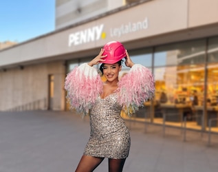 Leyla Heiter steht vor dem Penny Leylaland in Frankfurt und trägt ein Glitzerkleid und einen pinkfarbenen Bauhelm.
