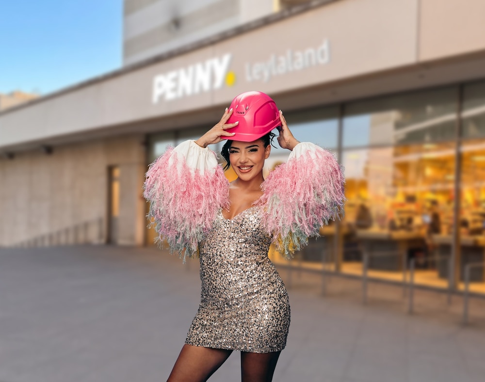 Leyla Heiter steht vor dem Penny Leylaland in Frankfurt und trägt ein Glitzerkleid und einen pinkfarbenen Bauhelm.
