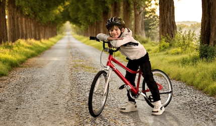 Junge steht mit rotem CRIVIT Kinderfahrrad von Lidl auf einem Weg