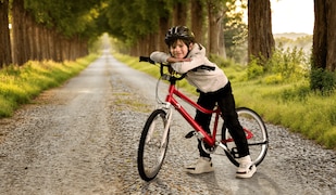 Junge steht mit rotem CRIVIT Kinderfahrrad von Lidl auf einem Weg