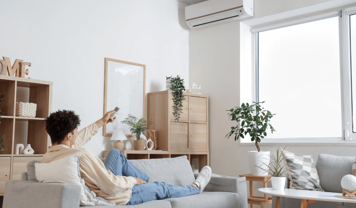 Mann liegt auf einer Couch und bedient eine Klimaanlage mithilfe einer Fernbedienung