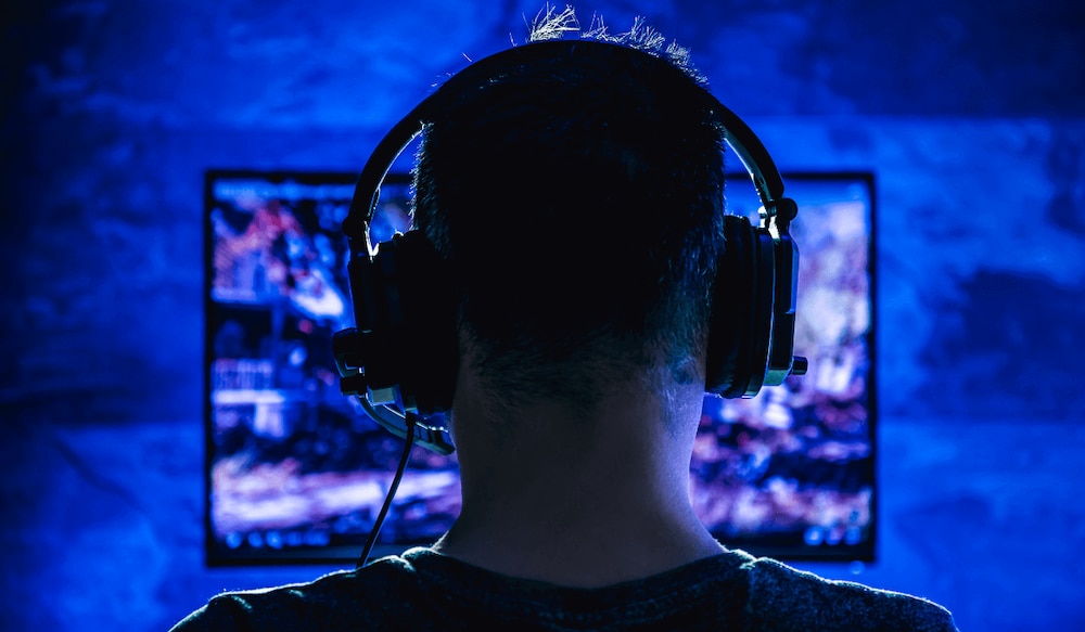 Mann sitzt mit Headset vor einem Bildschirm und spielt Videospiele