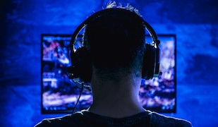 Mann sitzt mit Headset vor einem Bildschirm und spielt Videospiele