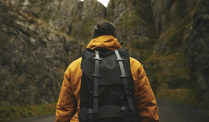 Mann trägt einen schwarzen Rucksack und läuft auf einen Berg zu
