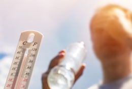 Mann trinkt bei Hitze Wasser mit einem Thermometer im Vordergrund