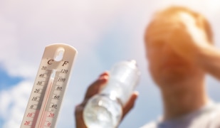 Mann trinkt bei Hitze Wasser mit einem Thermometer im Vordergrund