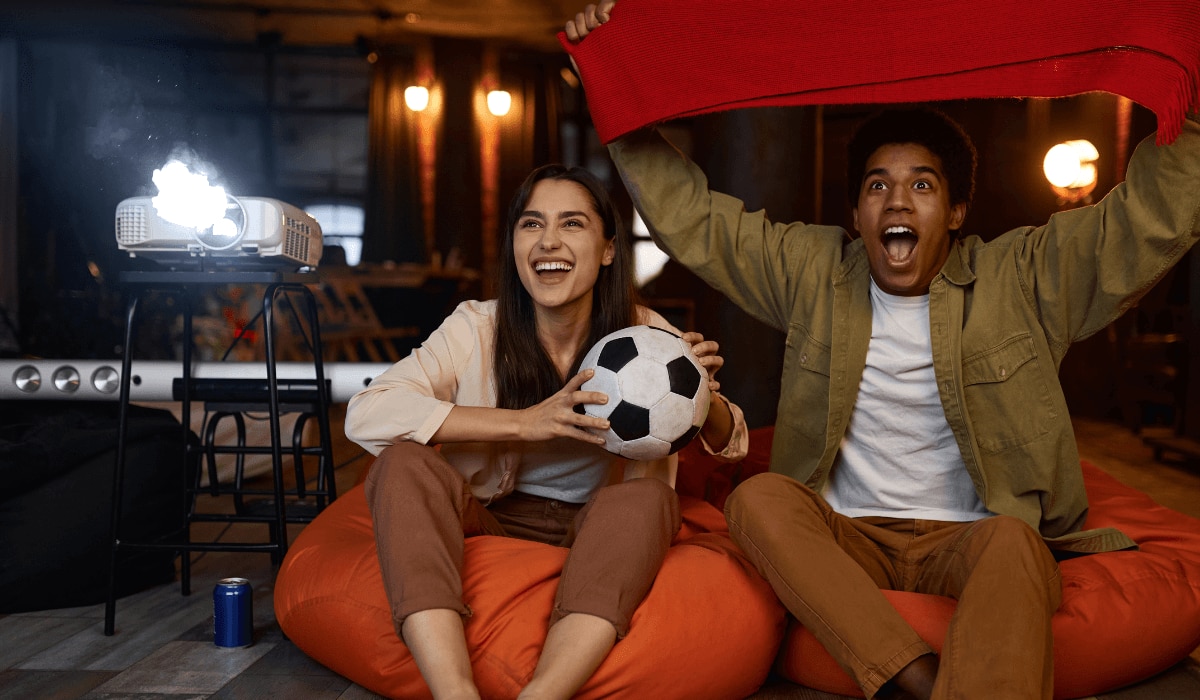 Menschen jubeln mit Fußball und einem Beamer im Hintergrund