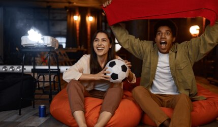 Mann und Frau gucken Fußball mit einem Beamer im Hintergrund