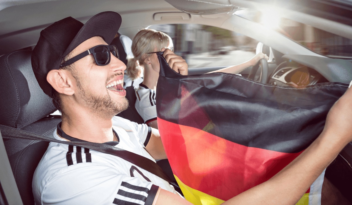 Mann und Frau sitzen mit Deutschlandflagge und Fußballtrikot im Auto und jubeln