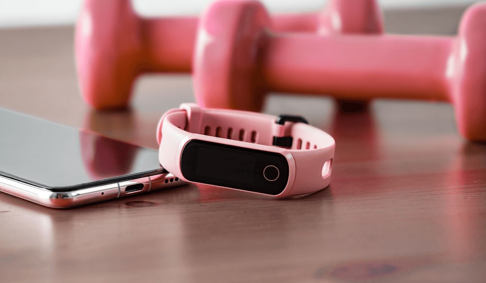 Pinker Fitness-Tracker neben Hanteln und einem Smartphone