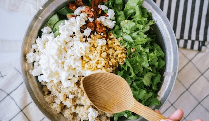 Silber Schüssel mit Quinoa, Feta, Salat, Gurke und einem Holzlöffel