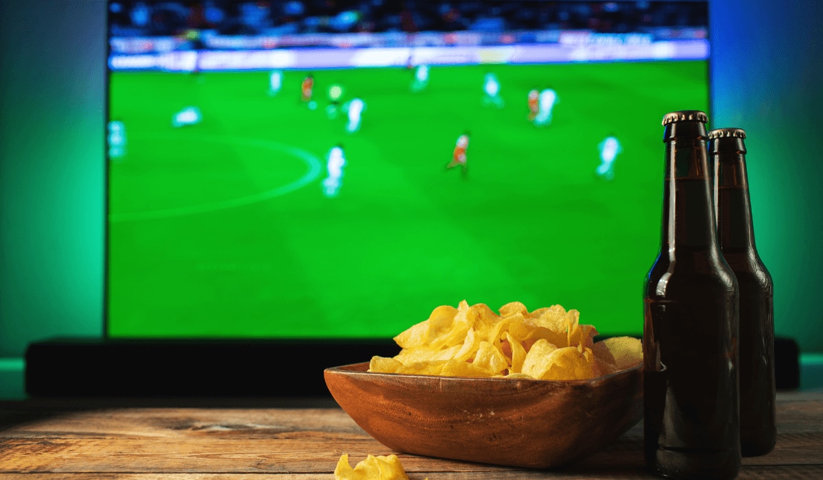 Snacks und Getränke vor einem Fernseher auf dem Fußball läuft