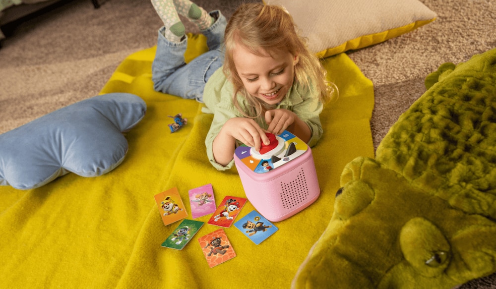 Mädchen spielt auf senfgelber Decke mit rosafarbener Toniebox